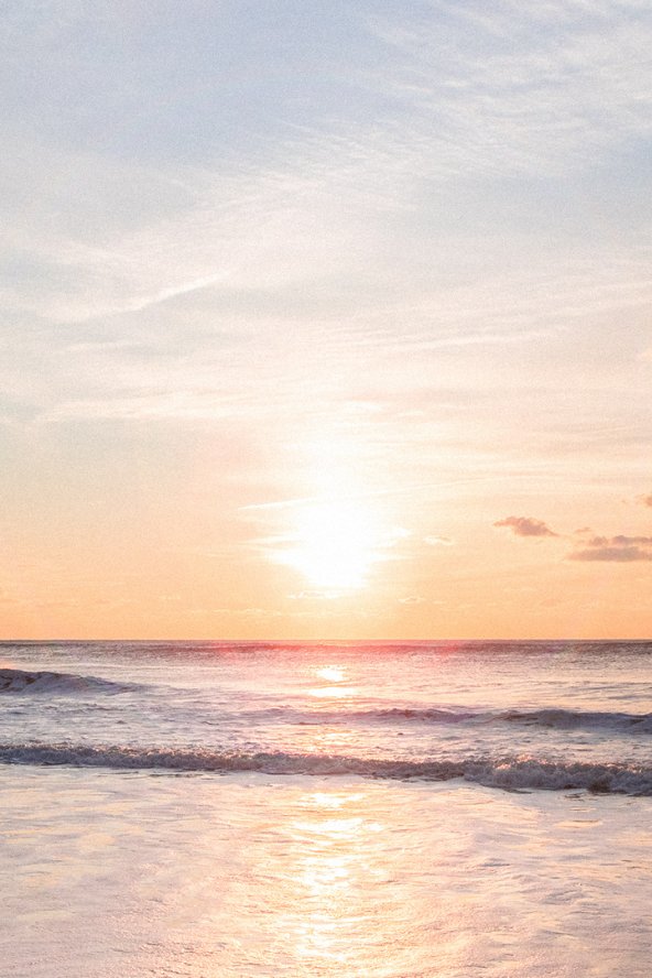 Sunset over a calm ocean, with soft pastel skies reflecting on gentle waves.
