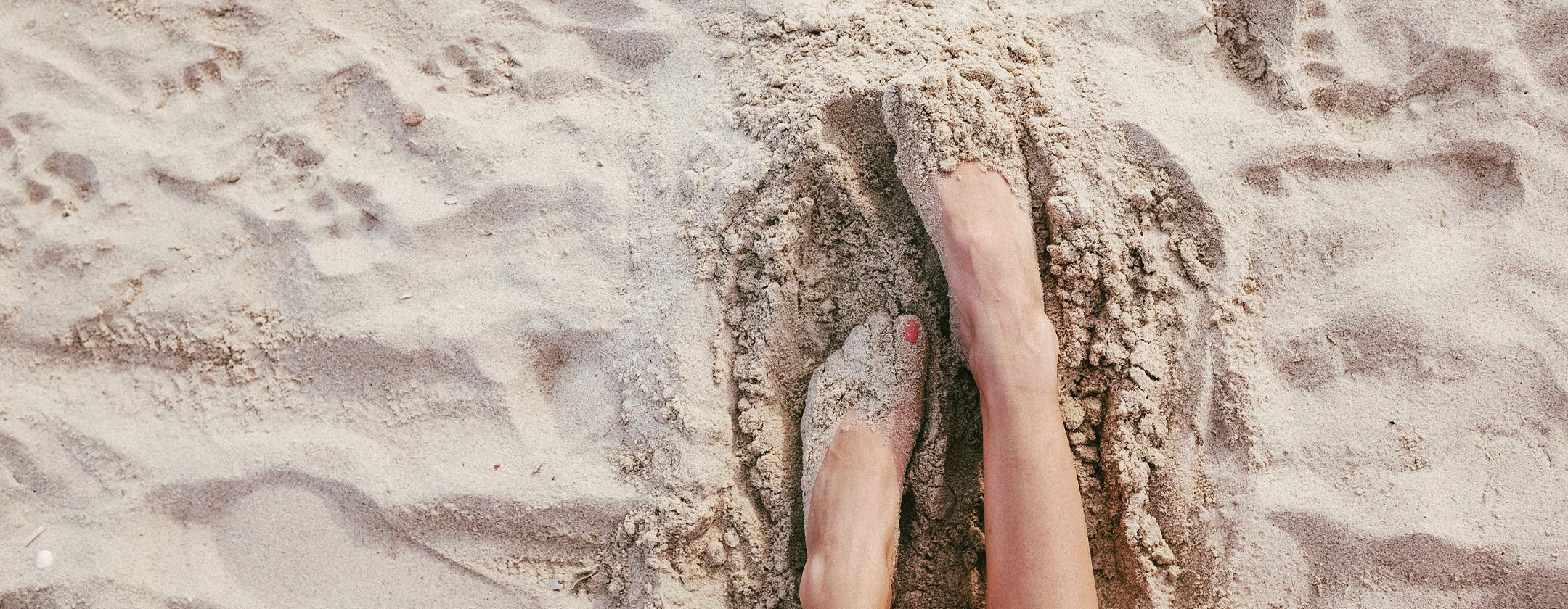 Feet partially buried in sand on a sunny beach.