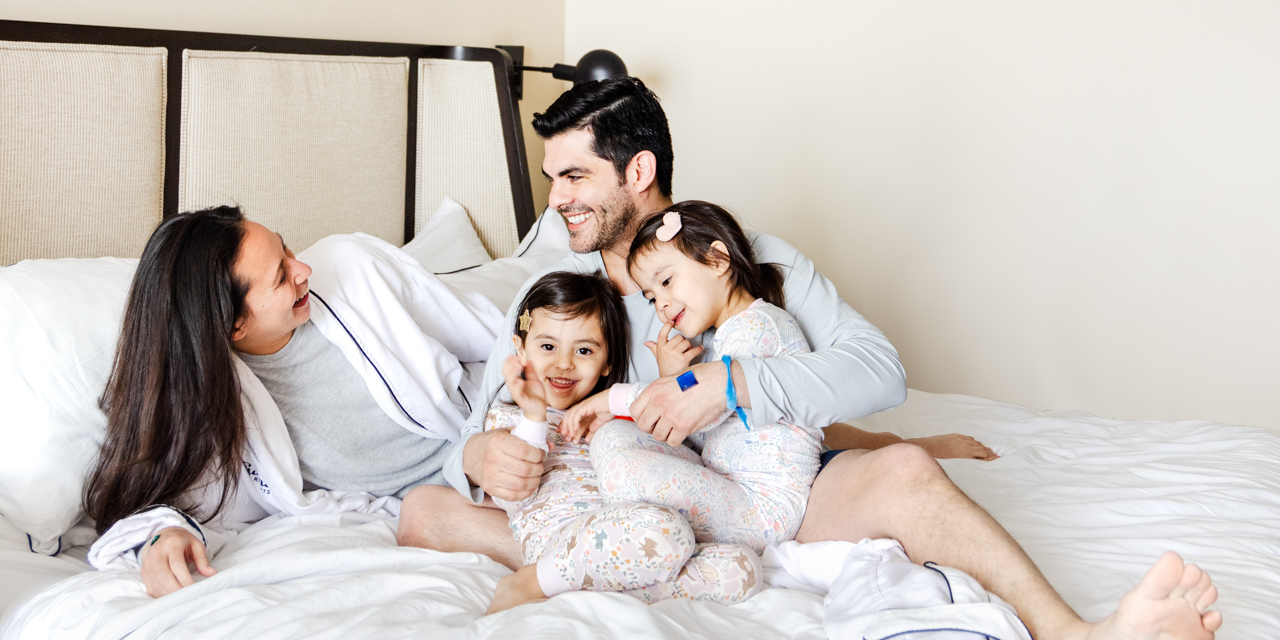 Husband and wife laughing in bed while cuddling with their two young daughters.