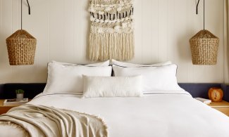 Cozy bedroom with a double bed, white linens, hanging woven lamps, and a macramé wall hanging above.