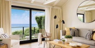 Cozy living room with a beach view, featuring neutral tones, a large round mirror, modern lamp, and black-and-white cushions on the sofa.