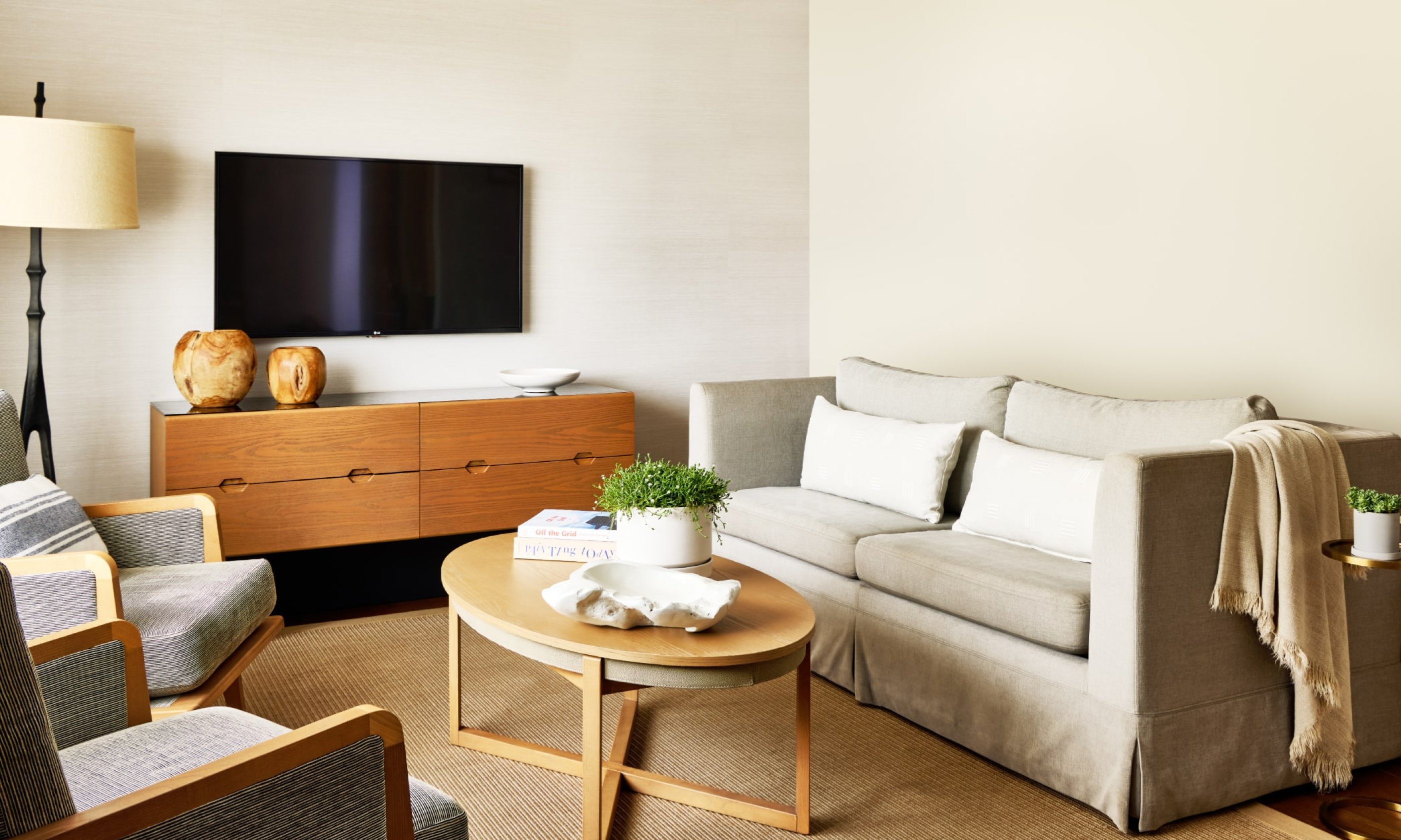 Modern living room with a beige sofa, wooden coffee table, flat-screen TV, and two armchairs. Neutral tones and minimalist decor enhance coziness.