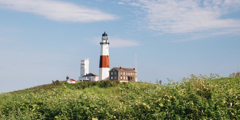Lighthouse with red and white stripes on a grassy hill under a partly cloudy sky.