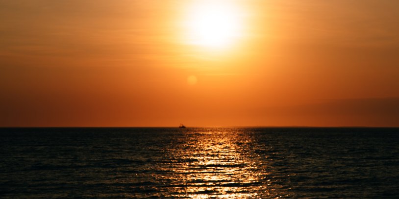 Sunset over the ocean with a glowing orange sky and shimmering reflections on the water.