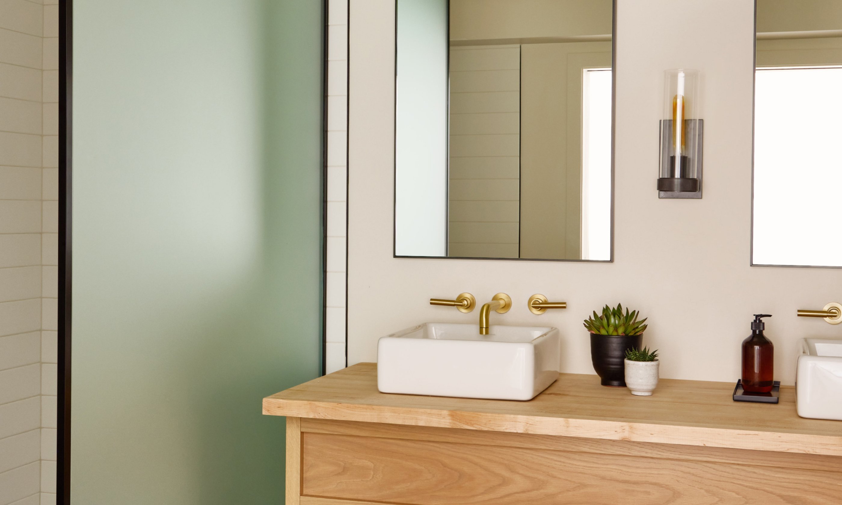 Modern bathroom with double sinks on a wooden counter, mirrors above, and a frosted glass shower door.