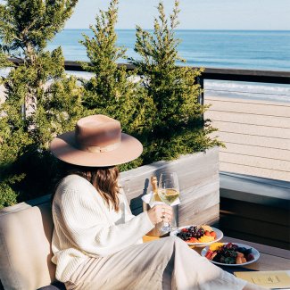 A woman in a hat looks out onto the ocean while holding a glass of white wine at 168极速赛车官方开奖结果记录体彩 Resort