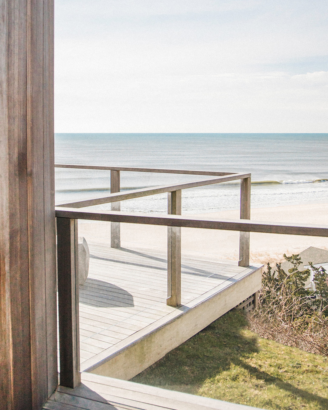 Wooden patio with chairs, facing the ocean in the background, surrounded by greenery and stone accents.