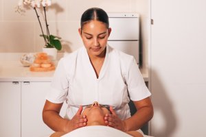 Female Spa Technician applying facial to relaxed guest with florals in background.