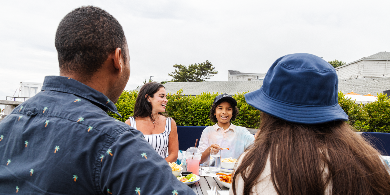 A family of four sits at a table enjoying a meal outdoors