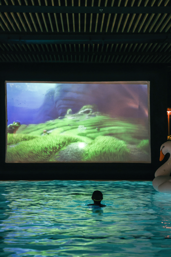 A child bobs in a pool in front of a bright screen