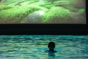 A child bobs in a pool in front of a bright screen