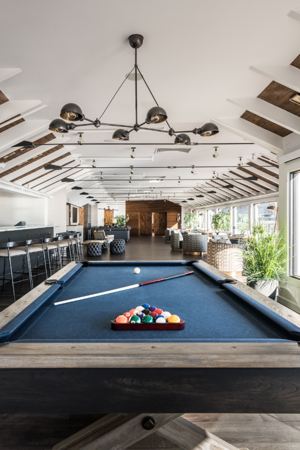 A pool table set with billiard balls in the foreground, with the Regent Lounge at Gurney's Montauk in the background.